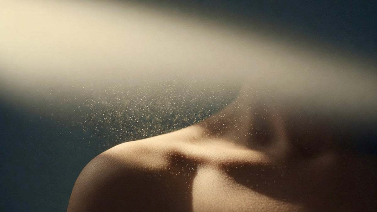 Fragrance mist settling on bare skin in warm directional light — the skin scent as base layer
